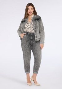 Džínsová bunda v bledě šedé barvě s předními kapsami, na sobě má hadí vzorovanou blůzu a šedé, zdrsněné džíny. Celý vzhled doplňují béžové lodičky.