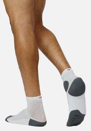 Weiße Knöchelsocken mit grauen Akzenten, die ein strukturiertes Mesh-Design, eine gepolsterte Sohle und ein kleines rotes Etikett nahe der Oberseite aufweisen.