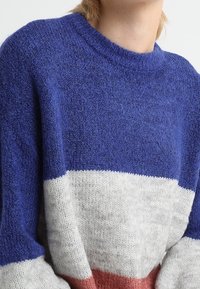 Blau-weißer und rostfarbener gestreifter Pullover mit strukturiertem Finish. Er hat einen runden Ausschnitt und eine lockere Passform, die weiche Fasern und kontrastierende Farben zur Geltung bringt.