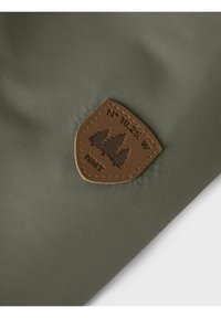 Olive zielony materiał o teksturowanej powierzchni, z brązową skórzaną łatą w kształcie tarczy, wytłoczoną z drzewami i współrzędnymi.