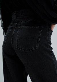 Jeans de mezclilla negra con cintura alta, diseño clásico de cinco bolsillos y sutiles detalles de costura en los bolsillos traseros.