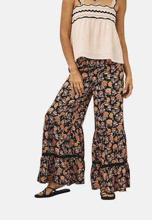 Pantalones palazzo negros con un estampado floral, con dobladillos con volantes y una cintura elástica, combinados con una camiseta sin mangas color crema con detalles en negro.