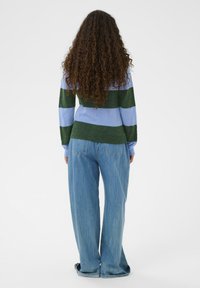 Pull rayé vert et bleu clair, avec des manches longues et une coupe décontractée, associé à un jean bleu clair ample. Cheveux texturés visibles.