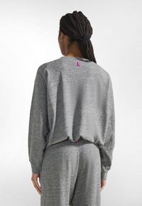 Sudadera gris con cuello redondo y puños acanalados, de corte holgado. Tiene una pequeña etiqueta rosa en la parte trasera cerca del cuello.