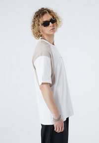 White and beige color-block oversized t-shirt with short sleeves, featuring a round neckline and side slit detail.