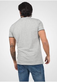 Camiseta corta de manga con textura gris y ribete negro en el cuello, combinada con jeans azul con costuras en forma de montaña en los bolsillos traseros.