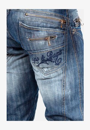 Donkerblauwe denim jeans met zichtbare stiksels, meerdere met rits afgesloten zakken en een geborduurd logo op de achterzak, met een gestructureerde afwerking.