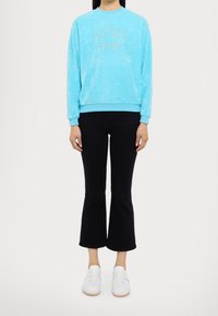 Sudadera de forro polar azul claro con la palabra "ACTIVE" en strass, combinada con jeans de campana negros y zapatillas blancas. Textura suave, corte relajado.