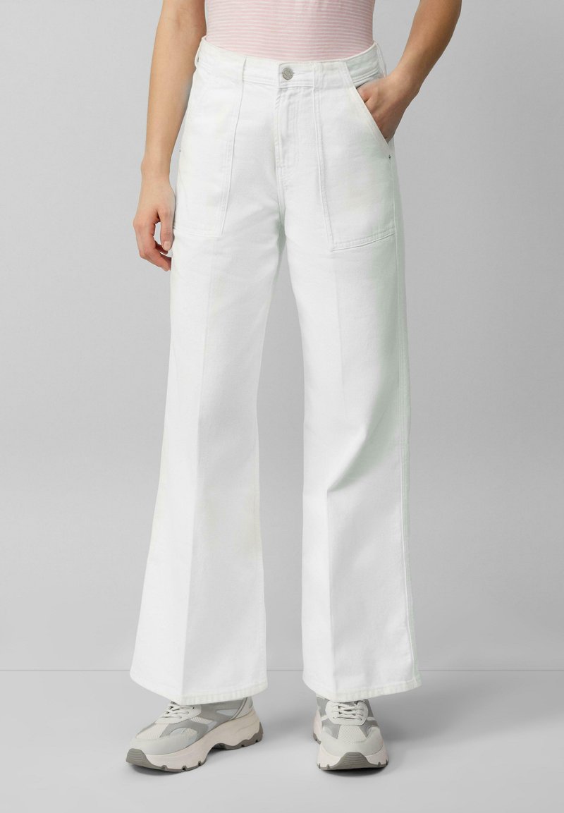Białe dżinsy w szerokim kroju, wykonane z denimu, z wysokim stanem, tylnymi i bocznymi kieszeniami oraz wyszywanym detalem. W zestawie z szarymi trampkami.