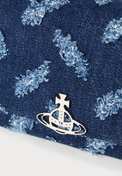 Denim tkanina s izblijeđenim mrljama koja ima srebrni grb s kuglom i križem te kružnim detaljima pričvršćenim blizu ruba.