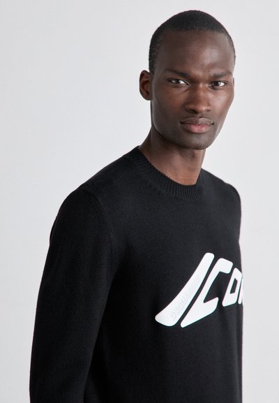 Sort strikket sweater med rund halsudskæring og stort hvidt "ICON" print på forsiden. Stoffet har en glat tekstur med ribbede manchetter.