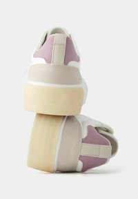 Bílé tenisky s texturovaným béžovým a světle růžovým podpatkem. Mají plochou, rýhovanou podrážku a látkový poutko vzadu.