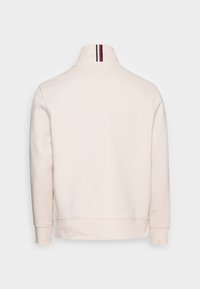 Krémová mikina s vysokým límcem, žebrovanými manžetami a pruhovaným akcentem na zadní straně límce. Měkká textura s uvolněným střihem.