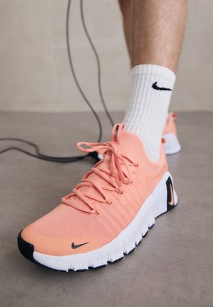 Personne portant des chaussettes blanches Nike et des baskets roses Nike avec des logos Swoosh noirs sur un sol gris, se préparant à sauter à la corde à sauter.