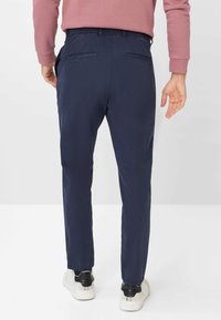 Pantaloni leggeri blu navy con vita elasticizzata, due tasche posteriori e design con gamba affusolata, abbinati a sneakers bianche.