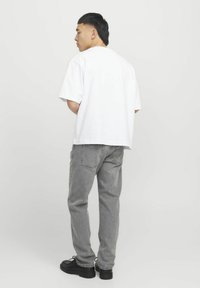 Witte oversized t-shirt met korte mouwen, gecombineerd met grijze denim jeans en zwarte schoenen. Eenvoudig ontwerp en neutraal kleurenschema.