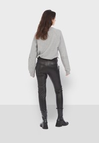 Šedá mikina s dlouhými rukávy, spárovaná s černými kalhotami z umělé kůže s vysokým pasem a kotníkovými botami na zip.