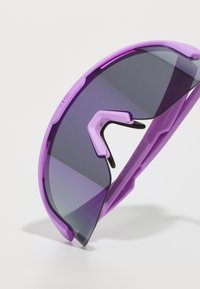 Lunettes de soleil violettes avec un design de lentille courbée, teinte dégradée sombre, monture en caoutchouc et caractéristiques ajustables pour un maintien sécurisé.