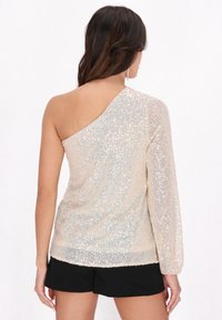 Paillettenoberteil in hellbeige mit einem langen Ärmel und einem schulterfreien Design. Verfügt über ein strukturiertes Strickmuster und schimmernde Details überall.