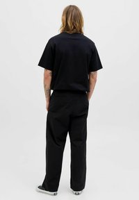 Sort T-shirt med afslappet pasform, korte ærmer og rund halsudskæring, parret med sorte bredbenede bukser og sorte sneakers.