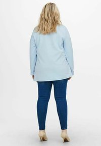 Light blue long-sleeve top, relaxed fit, with a round neckline. Paired with dark blue skinny jeans and beige heels. Plain texture.