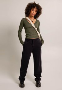 Olive green ribbed long-sleeve top, black jogger pants, and black lace-up boots. The top features an asymmetric neckline; pants have elastic waistband.