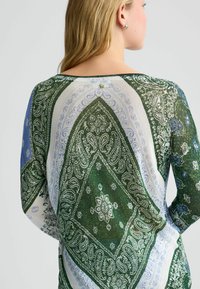 Groen en blauw gebreide trui met een paisleypatroon, ronde hals en een knoopaccent op de rug. Zachte, lichte stof.