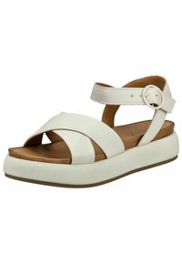 Bílé kožené sandály s designem křížem, nastavitelným páskem kolem kotníku a silnou bílou podrážkou. Obsahují hnědou stélku a kulatý kovový detail.