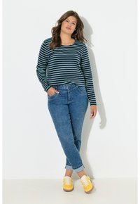 Pitkähihainen tummansininen ja petroolinsininen raidallinen paita yhdistettynä vaaleansinisiin farkkuihin; mallilla keltaiset tennarit, joissa valkoiset nauhat ja ruskeat pohjat.