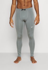 Leggings de sport gris en tissu extensible, présentant une coupe ajustée, une taille élastique avec cordon de serrage, et un logo Nike sur le côté.