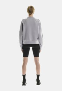 Sweatshirt gris clair avec un col rond, des manches raglan et un ourlet côtelé ; associé à un short de vélo noir et des baskets noires.