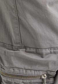 Tessuto grigio con una superficie liscia, caratterizzato da una tasca con zip ben visibile e dettagli cuciti lungo le cuciture per un tocco di design in più.