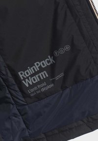 Tessuto di una giacca impermeabile nera con una trama liscia, caratterizzato da testo riflettente "RainPack Warm" e simboli per temperatura, acqua e protezione dal freddo.