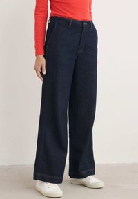 Breda ben mörk denimjeans med hög midja, kontrasterande sömmar, framfickor och en jämn yta, i kombination med vita sneakers.