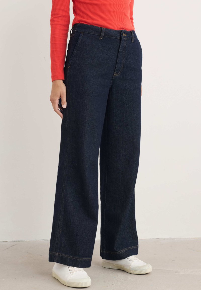 Breda ben mörk denimjeans med hög midja, kontrasterande sömmar, framfickor och en jämn yta, i kombination med vita sneakers.