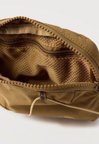 Καφέ θήκη με φερμουάρ ανοιχτή για να δείξει την εσωτερική θήκη από δίχτυ και την ύφανση ύφασμα, με ορατά τα δόντια του φερμουάρ και το τράβηγμα, σε λευκό φόντο.