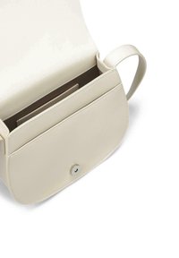 Bolso de mano de piel crema con un diseño redondeado y tapa plegable, que cuenta con un cierre magnético y una única correa para el hombro. El interior incluye compartimentos para tarjetas.