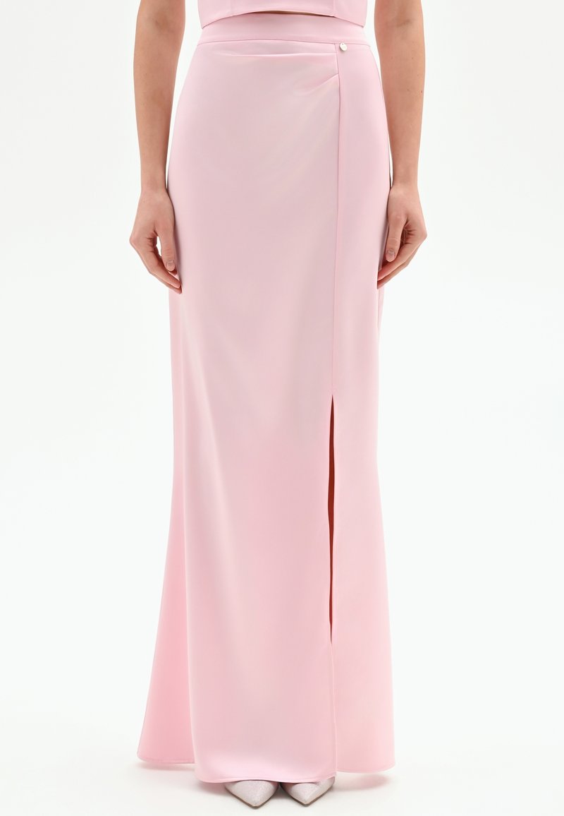 Lange, roze satijnen rok met een zijslit en een aangesloten tailleband, voorzien van een decoratieve knoopdetail op de heup. Gladde textuur.