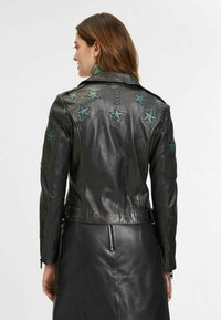 Veste en cuir noir avec des accents d'étoiles en teal, des manches texturées et une coupe ajustée. La vue arrière montre des détails de couture et de matériel.