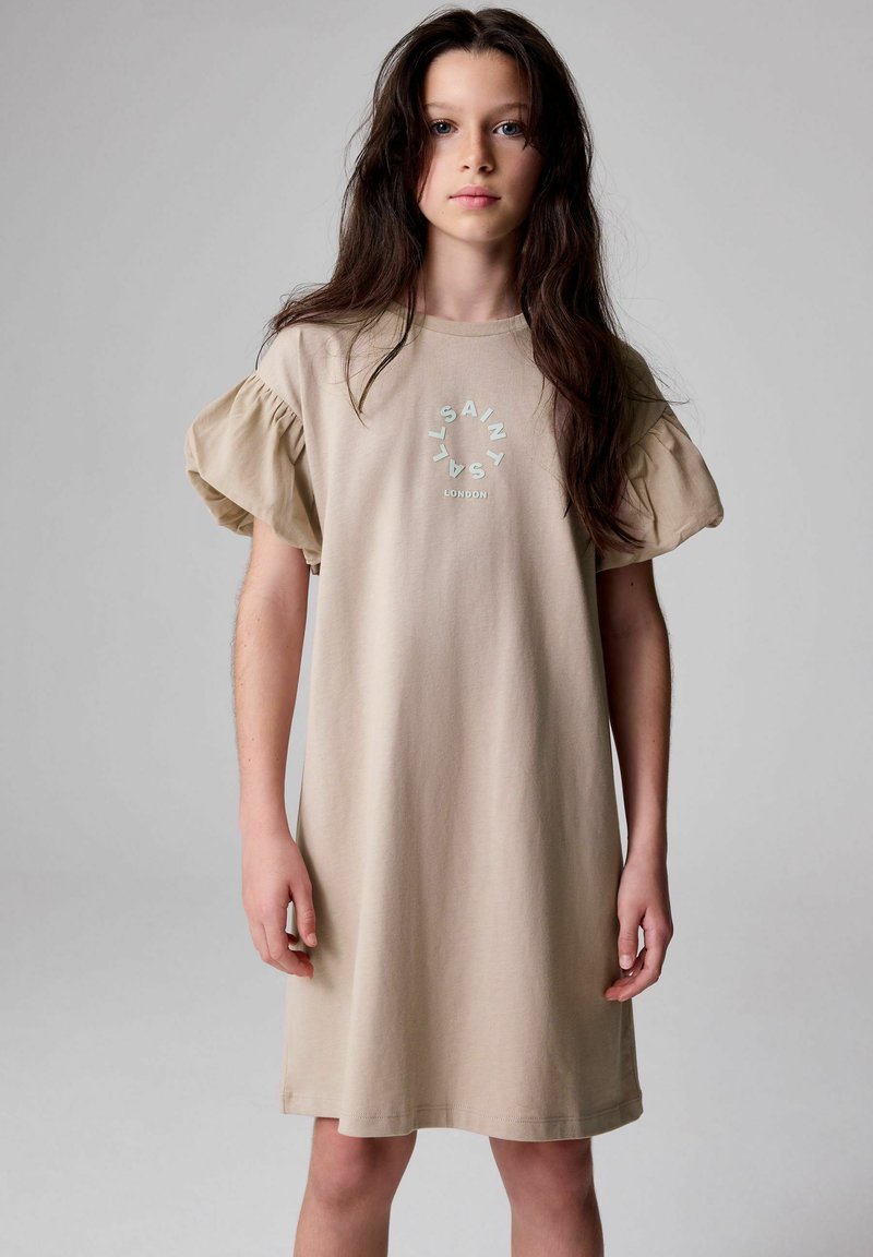 Beige bomullsklänning med kort puffärmar, med en cirkulär logotyp i ljusblått som har texten "SAINT LYS LONDON" på framsidan.