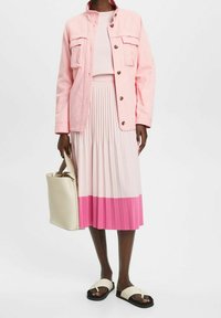 Veste en denim rose, robe côtelée assortie avec des plis et un dégradé de rose clair à rose foncé. Un sac à main beige et des sandales noires complètent le look.