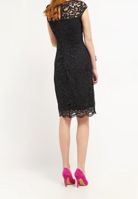 Svart spetsklänning med korta ärmar, intrikat blommönster och vågkant. Matchad med klarröda högklackade skor.