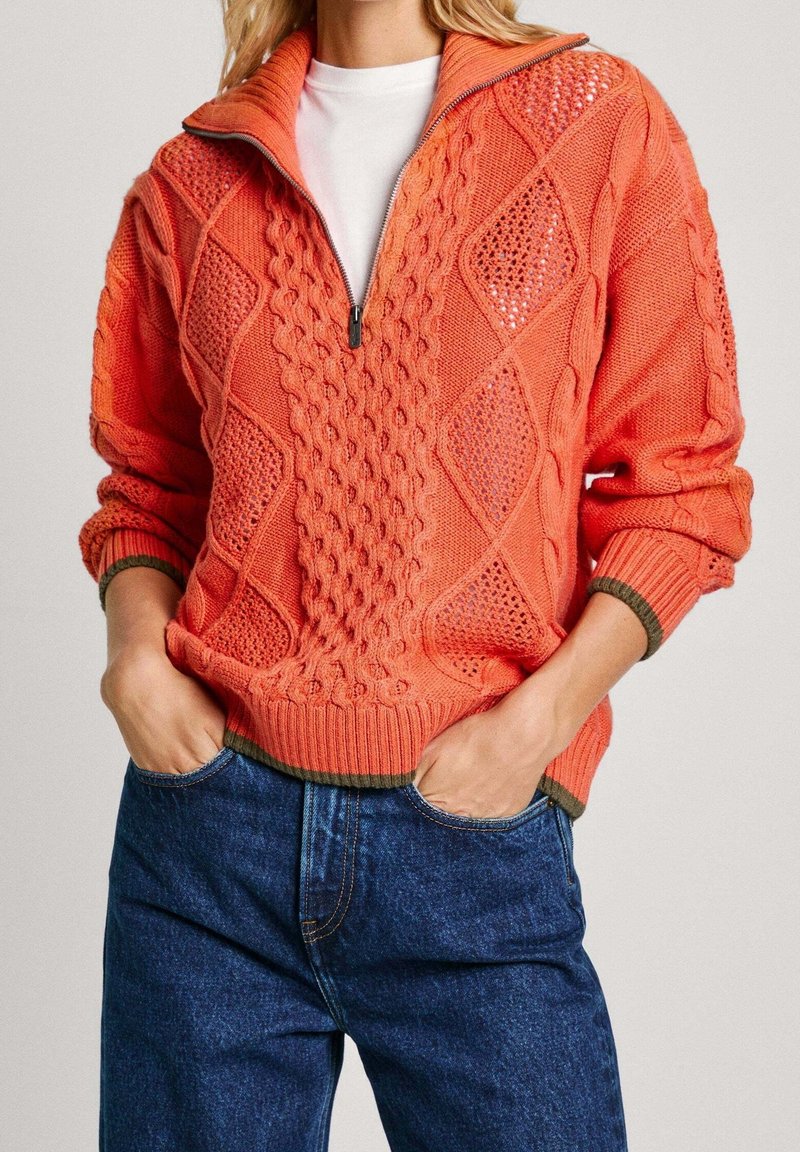 Suéter de punto naranja con cuello alto, que presenta patrones de rombos y texturas de punto cableado. Bajo y puños acanalados con un acento verde en contraste.