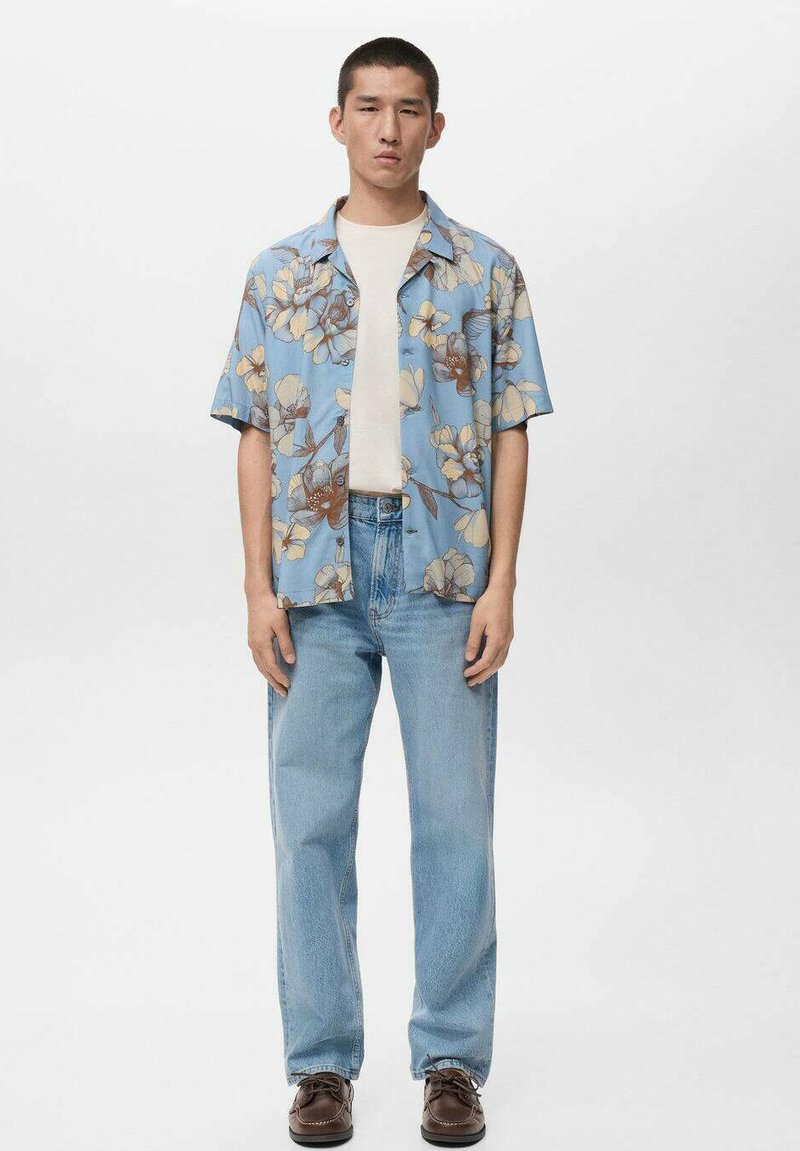 Kurzärmliges blaues Hemd mit floralem Muster, kombiniert mit einem hellen T-Shirt, hellblauen Jeans und dunkelbraunen Schuhen.