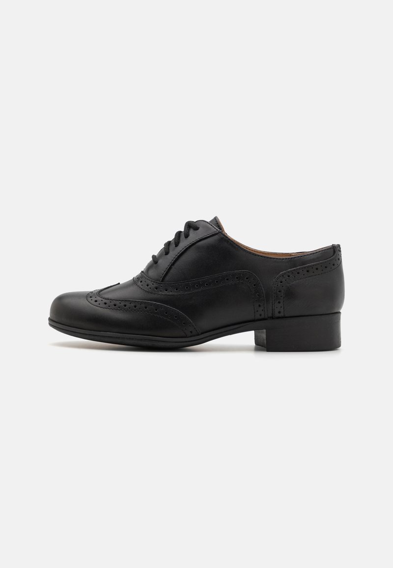 Chaussure brogue en cuir noir avec perforations en forme d'aile, petit talon et fermeture à lacets, vue de profil sur fond blanc.