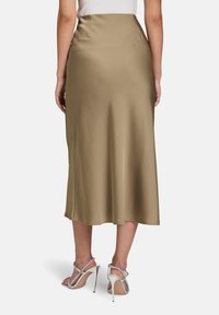 Khakifarbener Satin-Midrock mit glatter Textur, hoher Taille und seitlichen Taschen, kombiniert mit silbernen High-Heels.