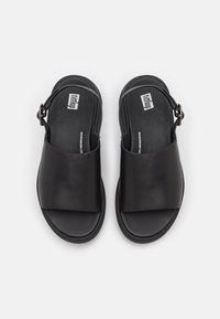 Mustat nahkasandaalit, joissa on leveä yläremmi ja takana nilkkaremmi, litteällä pohjalla ja minimalistisilla muotoiluelementeillä.