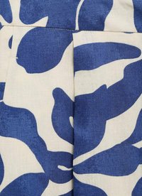 Stof met een crème achtergrond en blauwe abstracte bladerenpatronen. Het materiaal heeft een gestructureerde afwerking met subtiele schaduwwerking in het blauwe ontwerp.