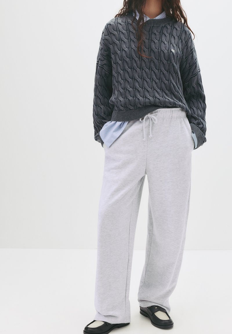 Grå kabelstrik sweater med rund hals lagd over en lyseblå stribet skjorte, sammen med grå sweatpants og sorte slip-on sko.
