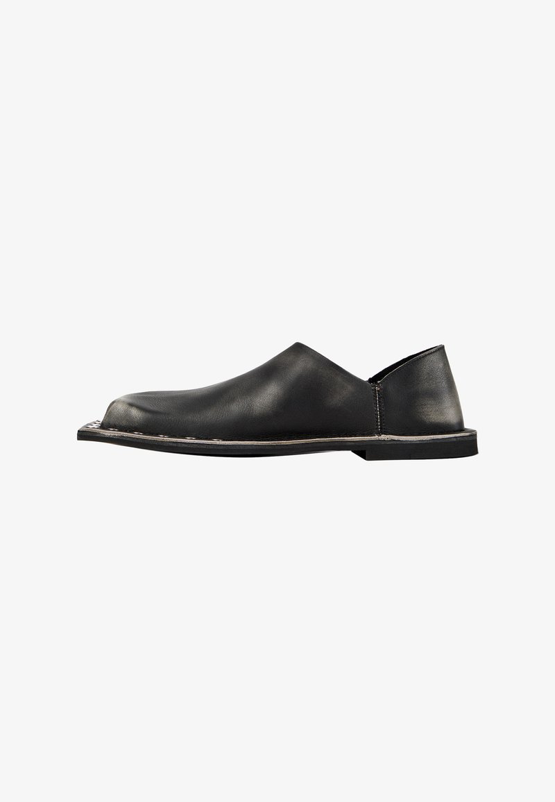Chaussure noire en cuir à enfiler avec semelle plate, bout arrondi et surpiqûres le long du bord, vue de profil sur fond blanc.